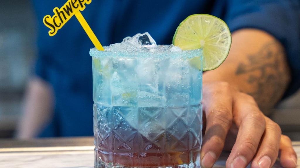 Cóctel con capas azul y roja, hielo, lima y agitador decorativo