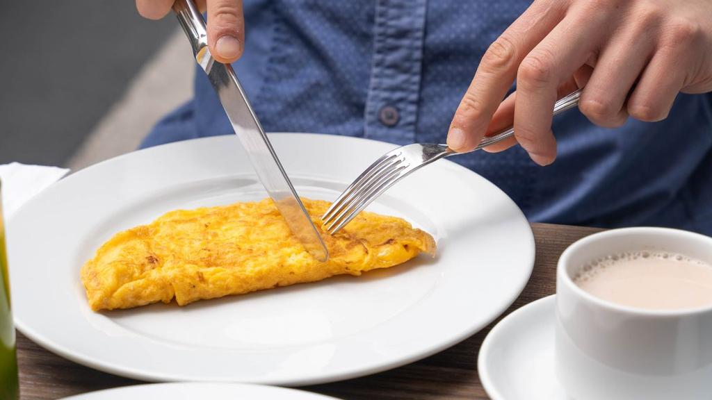 Omelette en plato blanco con café o té en mesa de desayuno