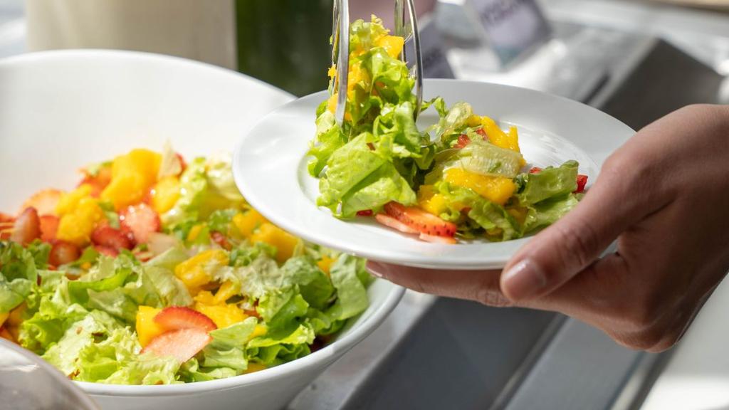Persona sirviendo ensalada fresca con frutas en plato blanco